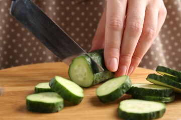 Woman cutting fresh cucumber at wooden board, closeup