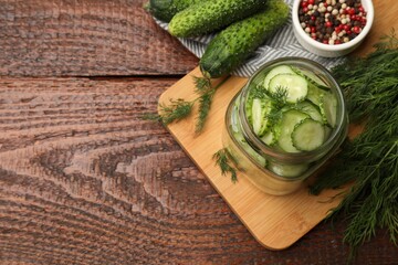 Making pickles. Slices of fresh cucumbers in open jar, dill and peppercorns on wooden table, flat lay. Space for text