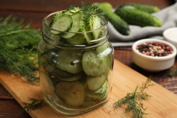 Making pickles. Slices of fresh cucumbers in open jar and dill on wooden table, closeup