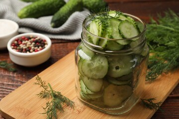 Making pickles. Slices of fresh cucumbers in open jar and dill on wooden table, closeup