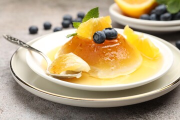 Tasty panna cotta with orange, blueberries and mint on light grey table, closeup