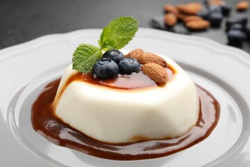 Tasty panna cotta with blueberries, almonds and sauce on black table, closeup