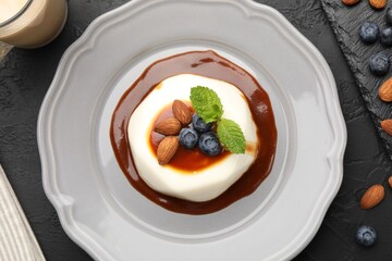 Tasty panna cotta with blueberries, almonds and sauce on black table, flat lay