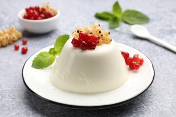 Tasty panna cotta with currants and mint on light grey table, closeup