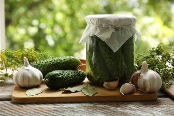 Making pickles. Fresh cucumbers in jar and spices on wooden table outdoors