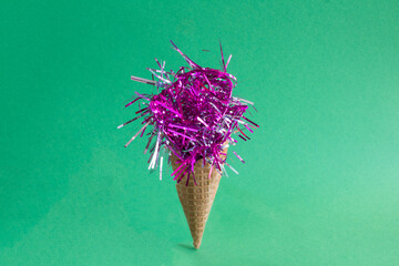 Ice cream cone with Сhristmas pink confetti on a green background. Close-up.