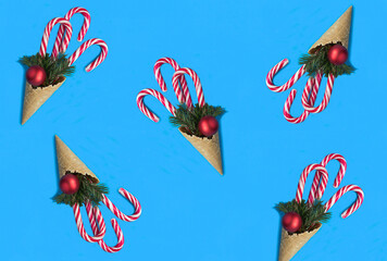 Ice cream cone with caramel canes, red balls and branches of spruce on a blue background. Сhristmas background. Flat lay.