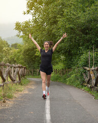 Young and beautiful girl, running with her arms raised, finishing the exercise, in a park surrounded by nature