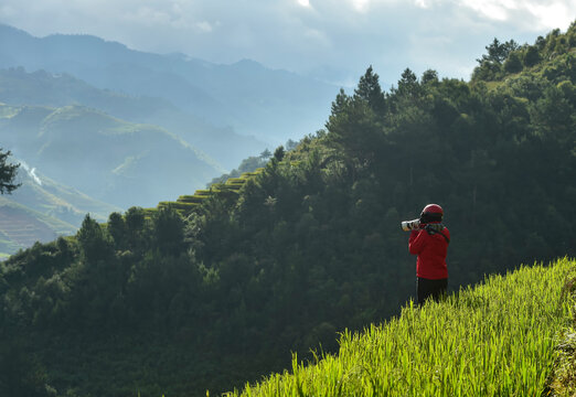 Fototapeta Rear view of a man wearing a helmet standing in a paddy field taking a photo with a telephoto lens, Mu Cang Chai, Yen Bai, Vietnam