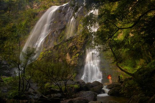 Woman with a parasol standing by Khlong Lan Waterfall, Khlong Lan National Park, Kamphaeng Phet Province, Thailand