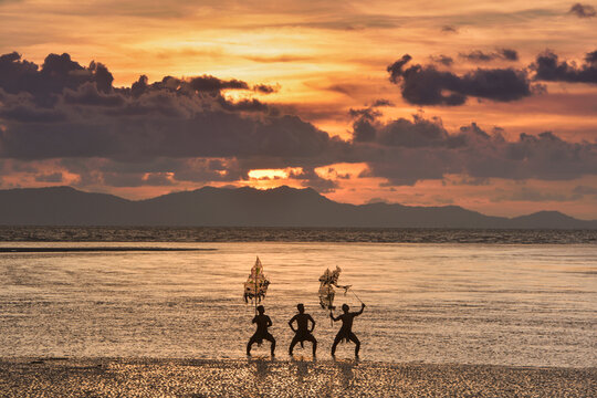 Silhouette of three men performing Traditional Thai Shadow Puppet Show (Nang Talung) on a beach at sunrise, Thailand