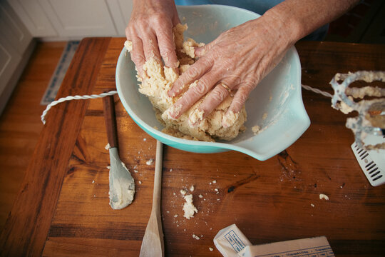 Close-up overhead view of a senior woman standing in a kitchen mixing cookie dough with her hands