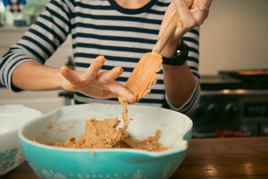 Close-up of a mid adult woman standing in a kitchen scraping off raw cookie dough from a spatula with her finger