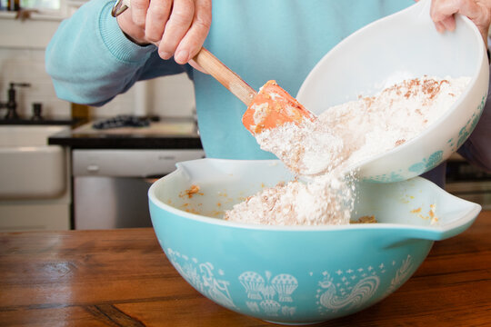 Close-up of a senior woman standing in a kitchen adding flour to a bowl to make cookies