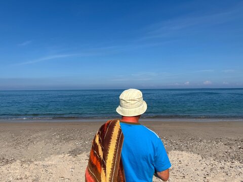 Rear view of a man on a beach in a t-shirt and hat carrying a towel ready to go swimming, Nordby, Samsoe, Jutland, Denmark