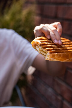 Close-up of a teenage boy's hand holding a half eaten grilled cheese panini sandwich