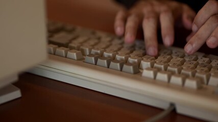 A close-up footage showing a person’s hands typing on a vintage beige computer keyboard connected to an old desktop computer. - Powered by Adobe