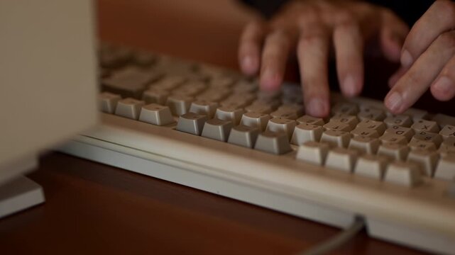 A close-up footage showing a person&rsquo;s hands typing on a vintage beige computer keyboard connected to an old desktop computer.
