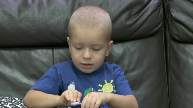 Child playing with new toy sitting on sofa at home. Concentrated face of little boy holding transformer robot toy. Three year old child examining new toy comments on his actions.