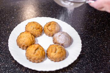 A baker dusts homemade muffins with powdered sugar, adding a subtle sweetness and decorative touch