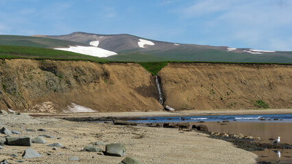 bering island. Scenic coastal landscape featuring a sandy beach, rocky shoreline, and a gentle...