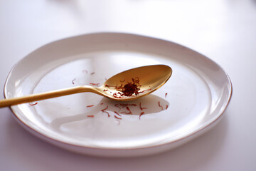 Golden spoon with saffron threads on white plate. Premium spice and gourmet presentation. Aromatic saffron on elegant spoon with white background.