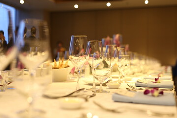 Elegant indoor banquet setup with warm lighting, neatly arranged glassware, folded napkins, and floral accents — perfect for a formal event or celebration.