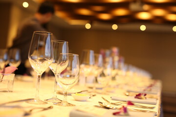 Elegant indoor banquet setup with warm lighting, neatly arranged glassware, folded napkins, and floral accents — perfect for a formal event or celebration.
