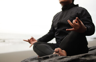 Young man meditating, practicing handstands, or lotus poses at sunset on the beach, ocean, or sea for mental health, mindfulness exercises, or chakra balancing.