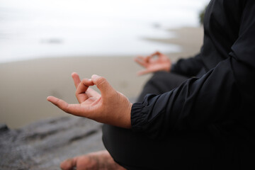 Young man meditating, practicing handstands, or lotus poses at sunset on the beach, ocean, or sea for mental health, mindfulness exercises, or chakra balancing.