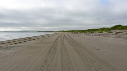 Tranquil beach scene featuring tire tracks in the sand leading towards the calm ocean under a...