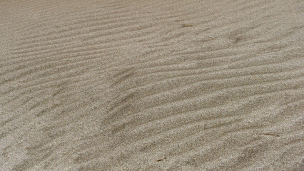 Textured sandy surface with gentle ripples and patterns created by wind, showcasing natural beauty and tranquility in a serene outdoor environment