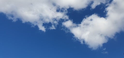 Soft, fluffy clouds drift gently across a bright blue sky, creating a natural background