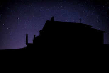 Obraz premium Silueta de una iglesia o edificio con una cruz en el techo, destacando contra un cielo estrellado. Imagen simbólica que evoca espiritualidad, reflexión y conexión con lo divino.