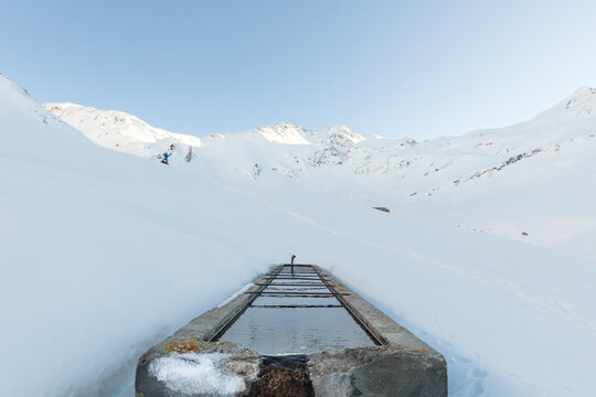 Water trough in snowy alpine valley with snowmobile in background