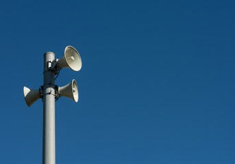 青空に立つ拡声器 四つ並ぶ白い筒 力強く響く声