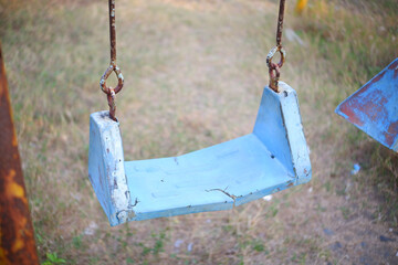 Broken plastic children's swing on the playground, old and unsafe swing. Old blue swing in an...