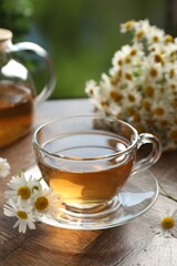 Aromatic tea in glass cup and chamomile flowers on wooden table, closeup