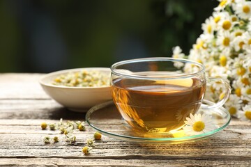Aromatic tea in glass cup and chamomile flowers on wooden table, closeup