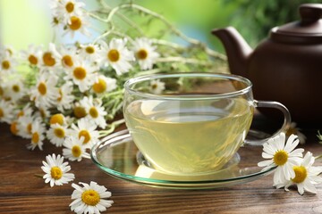 Tasty chamomile tea and flowers on wooden table, closeup