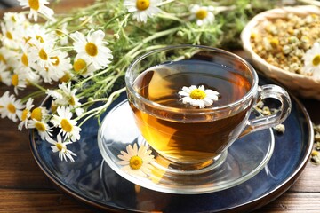 Tasty chamomile tea and flowers on wooden table, closeup