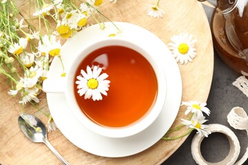 Tasty chamomile tea and flowers on black table, flat lay