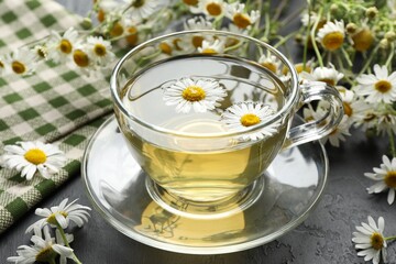 Tasty chamomile tea and flowers on black table, closeup