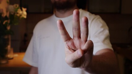 Man's hand displaying three fingers in a dimly lit room. Showing crown or trident with fingers