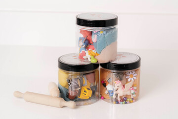 Creative playtime supplies in clear jars arranged on a white surface showcasing colorful materials,...