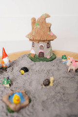 Miniature garden play scene with a whimsical house and colorful figurines in textured sand, perfect...