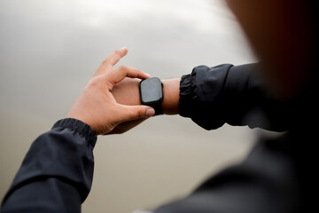 An athlete wears a smartwatch on his arm, is running and using an app. A male trainer in sportswear is on the beach.