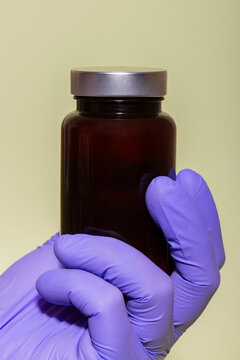 Gloved hand holding a dark glass jar with metal lid