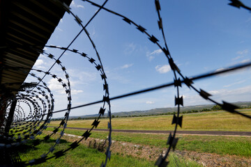 Barbed wire on fence, steel grating fence, metal fence wire. Coiled razor wire with sharp steel...