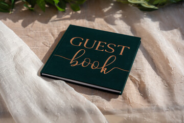 Elegant guest book resting on luxurious fabric surrounded by greenery